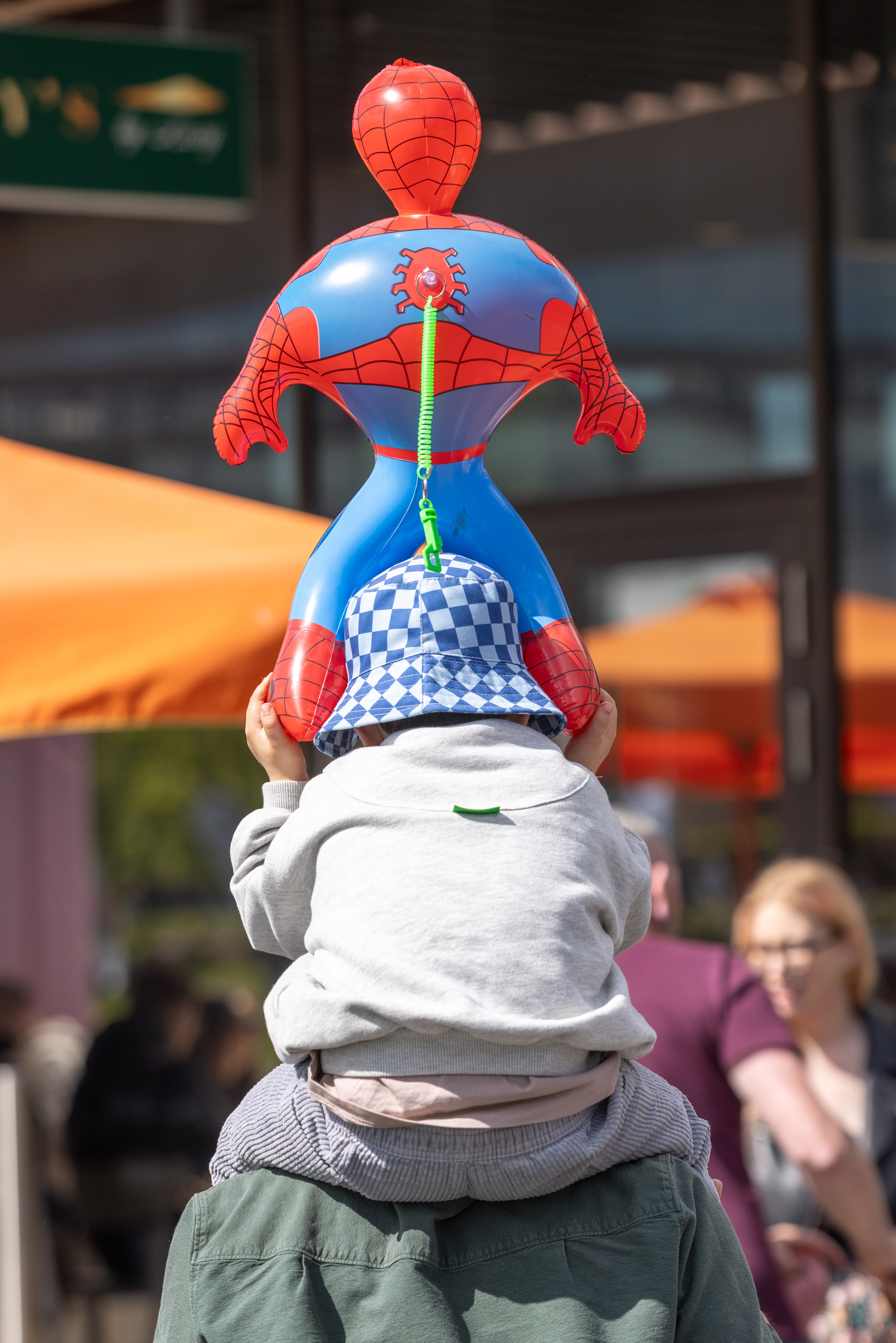 Child on parents shoulders holding a spiderman balloon. 